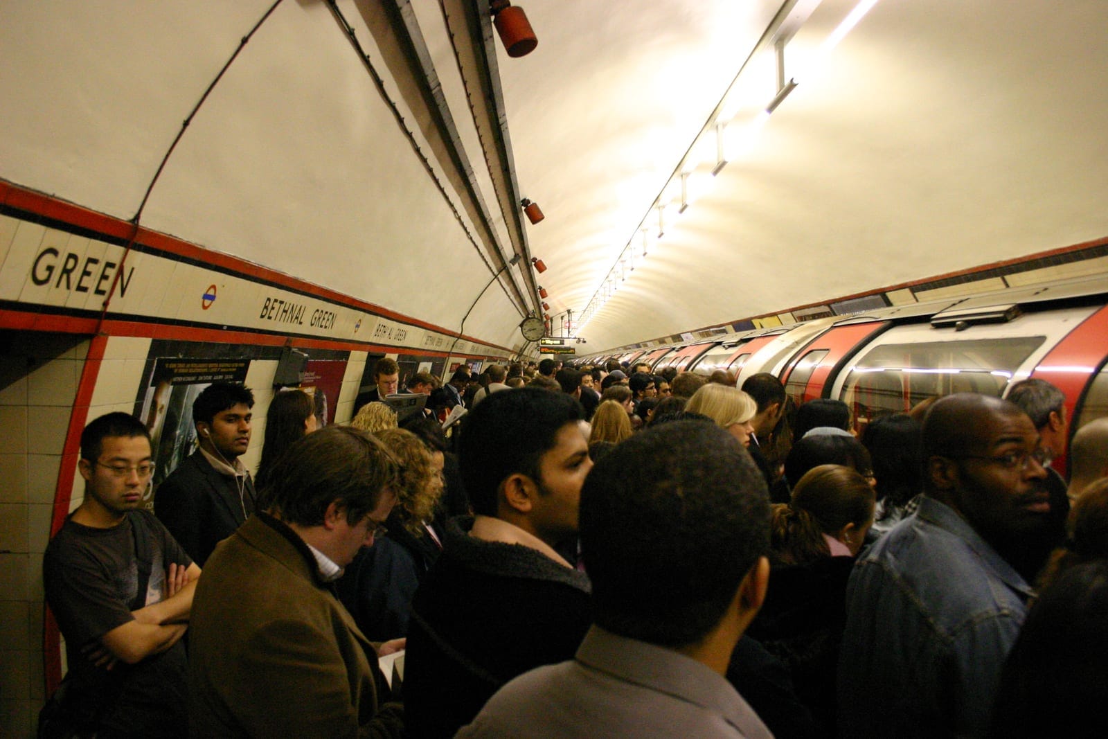 Des usagers attendent sur un quai du métro londonien, plusieurs portant des écouteurs