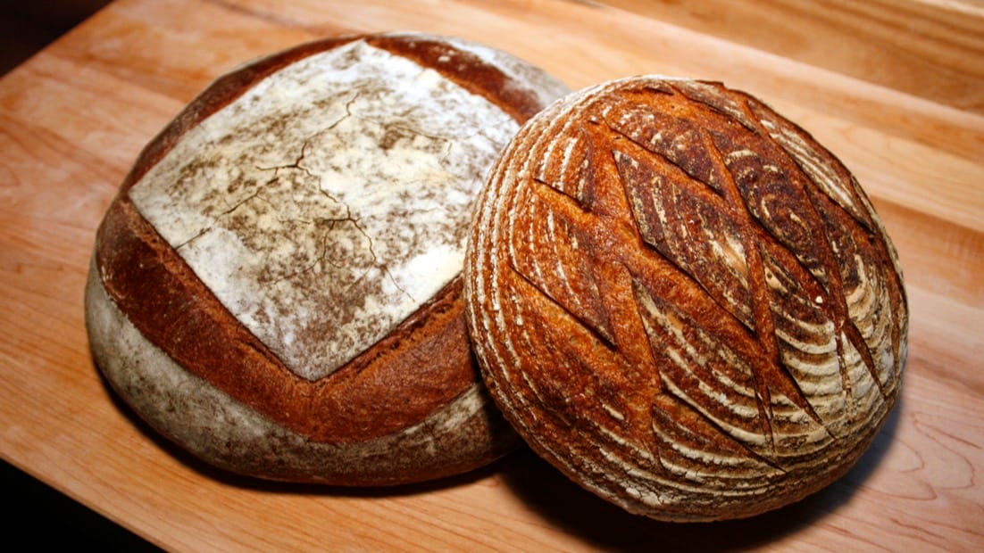 Une miche et une boule de pain au levain posées sur une planche en bois